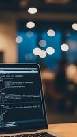 Laptop displaying programming code on screen in modern office environment with bokeh lights creating atmospheric workspace for software development.