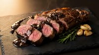 Grilled beef tenderloin steak sliced medium rare with dark sauce and herbs on slate board for gourmet dining and culinary presentations.