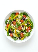 Fresh garden salad with tomatoes, cucumbers, bell peppers, spinach, olives and feta cheese on white plate, overhead view for healthy eating and nutrition content.