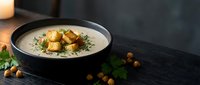 Creamy mushroom soup with golden croutons and fresh herbs in elegant black bowl on dark wooden surface for gourmet dining and culinary presentations.