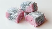 Pink and silver Turkish delight pieces on white background, traditional Middle Eastern confectionery with metallic foil wrapping showing soft texture and sweet appeal.