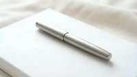 Elegant silver metallic pen lying on white paper notebook with soft fabric background for professional writing and business documentation.
