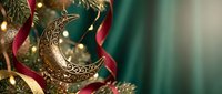 Ornate golden crescent moon decoration with intricate patterns among festive ribbons and pine branches creating elegant holiday atmosphere with warm bokeh lights.