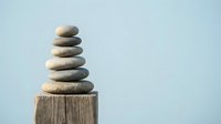 Balanced stack of smooth river stones on weathered wooden post against soft blue sky background for meditation wellness and mindfulness concepts.