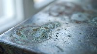 Weathered copper surface with green patina oxidation and water droplets showing natural aging process and corrosion effects on metal material.