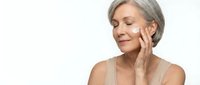 Mature Caucasian woman applying anti-aging cream to face with gentle touch, skincare routine for healthy glowing skin on white background.