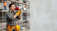 Construction worker with megaphone announcing sale at building site. Male contractor in plaid shirt and tool belt shouting promotional message on construction background.