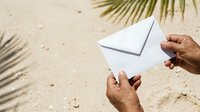 Hands holding blank envelope on sandy beach with palm shadows, suitable for summer correspondence, travel mail, vacation messages, and seasonal communication concepts.