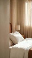 Serene bedroom corner with white pillows and bedding on wooden frame, warm sunlight filtering through beige curtains, minimalist interior design for relaxation.