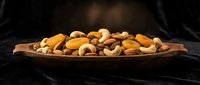 Mixed nuts and dried fruits arranged on rustic wooden plate against dark background for healthy snacking and gourmet food concepts.