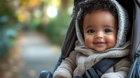 Adorable African American baby with bright smile wearing cozy winter hoodie sitting in stroller outdoors. Natural bokeh background creates warm atmosphere.