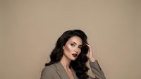 Professional brunette businesswoman in beige suit with dark lipstick posing confidently against neutral background for corporate branding and marketing.