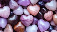Collection of polished heart-shaped gemstones in various shades of pink, purple, and white, arranged together for crystal healing or spiritual practices.