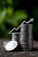 Stacked silver coins with upward trending arrow symbol against green natural background, representing financial growth and investment success in business.