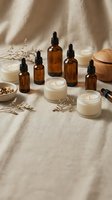 Amber dropper bottles, soy candles, and a wood diffuser arranged on linen with dried herbs for a natural wellness flat lay.
