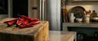 Fresh red chili peppers on wooden cutting board in modern kitchen interior ready for cooking spicy dishes and culinary preparations.