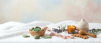 Spa wellness setup with essential oil diffuser, lavender, eucalyptus leaves and honey on white linen for relaxation and aromatherapy treatments.