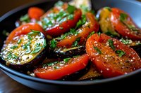 Fresh red tomato slices garnished with herbs, spices and olive oil on dark plate, close up view of appetizing Mediterranean cuisine served as starter.