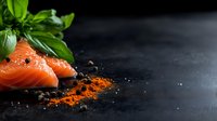 Fresh raw salmon fillet with basil leaves, black peppercorns and paprika powder on dark background. Minimalist food composition with copy space.