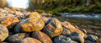 Smooth river rocks and pebbles on shoreline with flowing water in background, natural stone texture for landscaping and zen garden design projects.