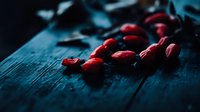 Fresh red cranberries scattered on dark wooden surface in moody lighting with shallow depth of field, creating dramatic food photography atmosphere.