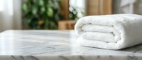 Rolled white towel on marble surface with blurred spa background, suitable for wellness, hospitality and bathroom product marketing.