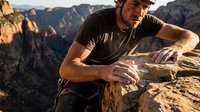 Middle-aged Caucasian male rock climber resting on sandstone cliff edge during golden hour sunset in desert canyon landscape for outdoor adventure sports.