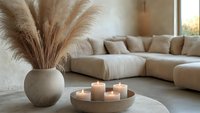 Minimalist living room interior with pampas grass in concrete vase and burning candles on coffee table. Cozy modern home decor with beige sectional sofa.