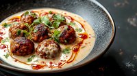 Gourmet meatballs with creamy sauce and herbs served in elegant ceramic bowl, restaurant-style plating for culinary photography and food marketing.