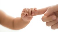 Tiny newborn hand gripping an adult finger, symbolizing trust, love, and family bond on a soft white background.