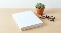 White blank book cover mockup on wooden desk with succulent plant and eyeglasses for branding design presentation and publishing projects.