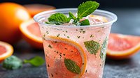 Fresh citrus cocktail with grapefruit juice, orange slice, mint leaves and ice in plastic cup on dark background, refreshing summer drink.