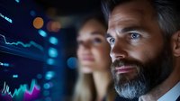 Middle-aged Caucasian businessman with beard analyzing financial data charts on digital screens in modern trading office environment.