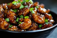 Glazed shrimp in sweet and savory Asian sauce garnished with fresh chopped green onions served in black ceramic bowl, close up view of appetizing seafood dish.