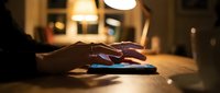 Hands typing on smartphone in warm evening light at home office desk creating cozy atmosphere for digital communication and mobile technology use.