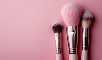 Professional makeup brushes with soft pink bristles and metallic handles arranged on pink background, minimal beauty concept for cosmetics and skincare advertising.