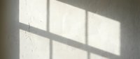 Natural sunlight streaming through window creates geometric shadow patterns on textured white wall surface for interior design and architecture concepts.