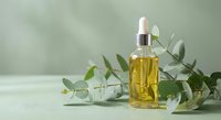 Natural eucalyptus essential oil in glass dropper bottle with fresh green leaves on neutral background for aromatherapy and wellness products.