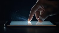 Hand touching glowing tablet screen in dark environment with magical sparkle effect and blue light emission, modern technology concept for digital interaction.