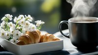 Fresh baked croissant served with hot steaming coffee and white flowers in modern setting, morning breakfast composition with natural light and bokeh.
