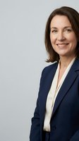 Professional middle-aged Caucasian businesswoman in navy blue suit smiling confidently against neutral background for corporate marketing materials.
