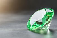 Brilliant cut emerald gemstone with facets reflecting light on gray surface, showcasing luxury and precision craftsmanship in jewelry design and precious stones.
