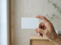 Mature man with medium skin tone holding blank white business card in hand, displaying mockup template for branding and corporate identity design projects.