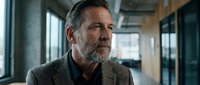 Middle-aged man with gray beard and salt-and-pepper hair wearing casual blazer in modern office corridor with natural light, suitable for corporate, business, and professional lifestyle content.