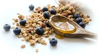 Granola cereal with fresh blueberries and honey drizzle on wooden spoon, overhead flat lay composition for breakfast and healthy eating content.
