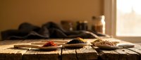 Wooden spoons filled with colorful spices arranged on rustic table in warm kitchen lighting for cooking and culinary preparation.
