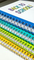 Stack of colorful spiral-bound notebooks with back to school text on white cover, featuring blue, teal and yellow binding rings for education supplies.