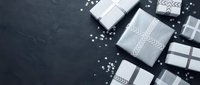 Elegant gift boxes in black, white and gray with ribbons and decorative pearls arranged on dark slate background for special occasions and celebrations.
