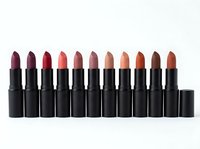 Row of colorful lipsticks in black tubes displaying various shades from deep burgundy to nude tones arranged on white background for cosmetic branding.