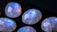 Iridescent rainbow moonstone gems with holographic surface reflecting blue and purple light on dark background for jewelry design and luxury accessories.
